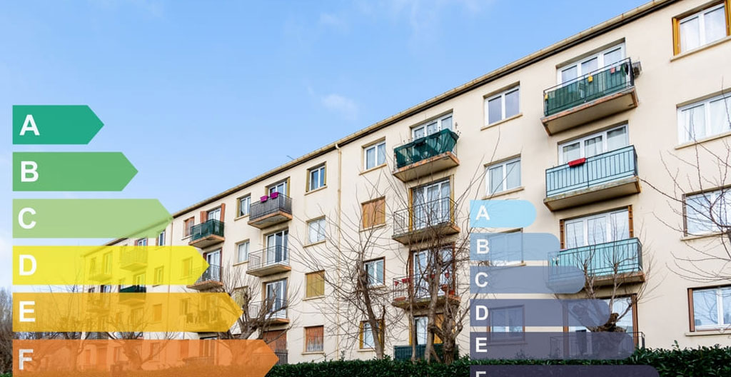 Façade d'un immeuble collectif des années 1970-80 vue depuis la rue, avec des radiateurs visibles derrière les fenêtres sous un ciel gris